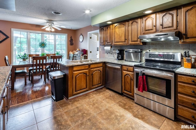 1814 Testa Dr, Marion, IL 62959 - kitchen featuring stainless steel appliances, under cabinet range hood, a peninsula, brown cabinets, and a textured ceiling