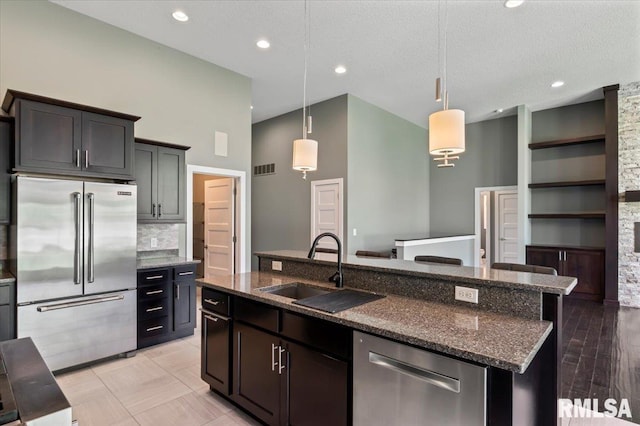 6691 Spring Creek Dr, Bettendorf, IA 52722 - kitchen with stainless steel appliances, a kitchen island with sink, dark stone counters, pendant lighting, and a textured ceiling