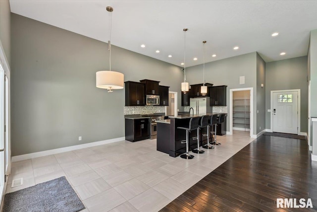 6691 Spring Creek Dr, Bettendorf, IA 52722 - kitchen featuring appliances with stainless steel finishes, a high ceiling, a kitchen breakfast bar, a kitchen island with sink, and hanging light fixtures