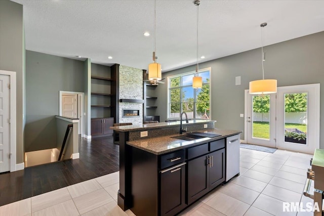 6691 Spring Creek Dr, Bettendorf, IA 52722 - kitchen with dishwasher, a stone fireplace, a kitchen island with sink, pendant lighting, and dark stone countertops
