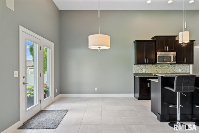 6691 Spring Creek Dr, Bettendorf, IA 52722 - kitchen with stainless steel microwave, backsplash, dark brown cabinetry, pendant lighting, and a high ceiling