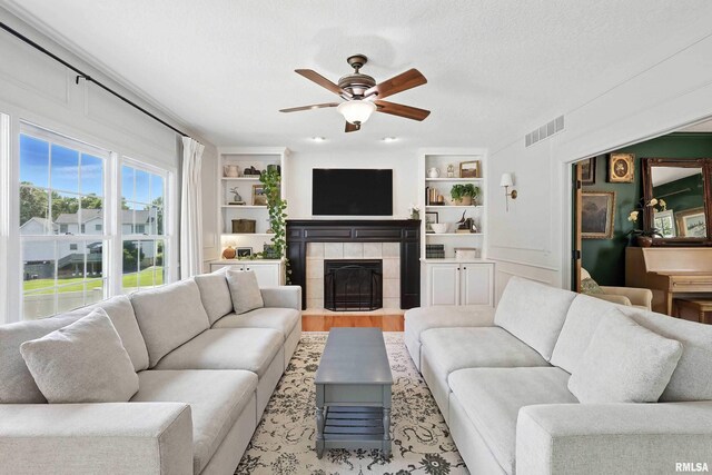 1200 Bridgeview Place, Le Claire, IA 52753 - living room featuring ceiling fan, built in shelves, a tile fireplace, and a textured ceiling