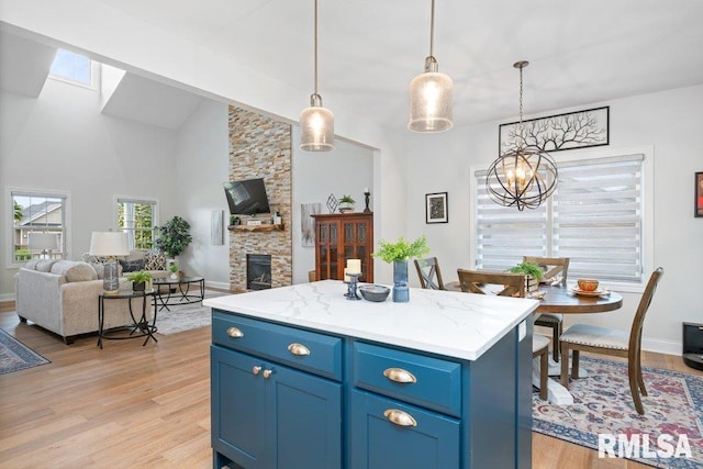 1100 Wild W Dr, Le Claire, IA 52753 - kitchen featuring blue cabinetry, a chandelier, open floor plan, light wood-type flooring, and a stone fireplace