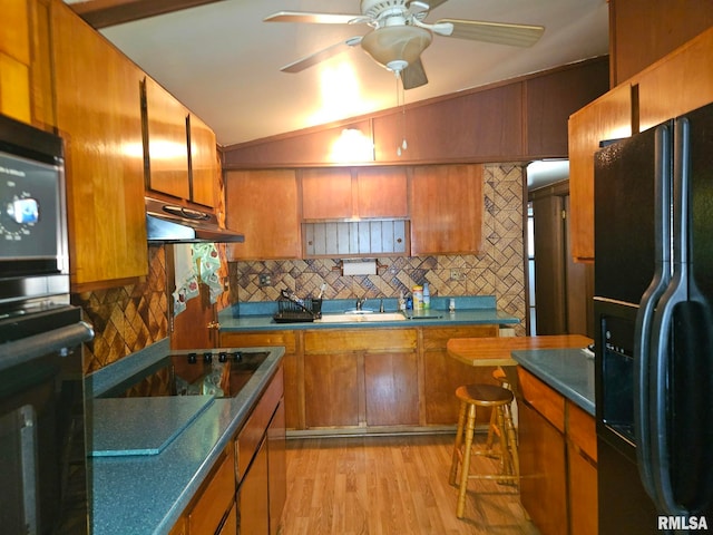 509 W 9th St, Tipton, IA 52772 - kitchen with black appliances, under cabinet range hood, brown cabinetry, tasteful backsplash, and light wood finished floors