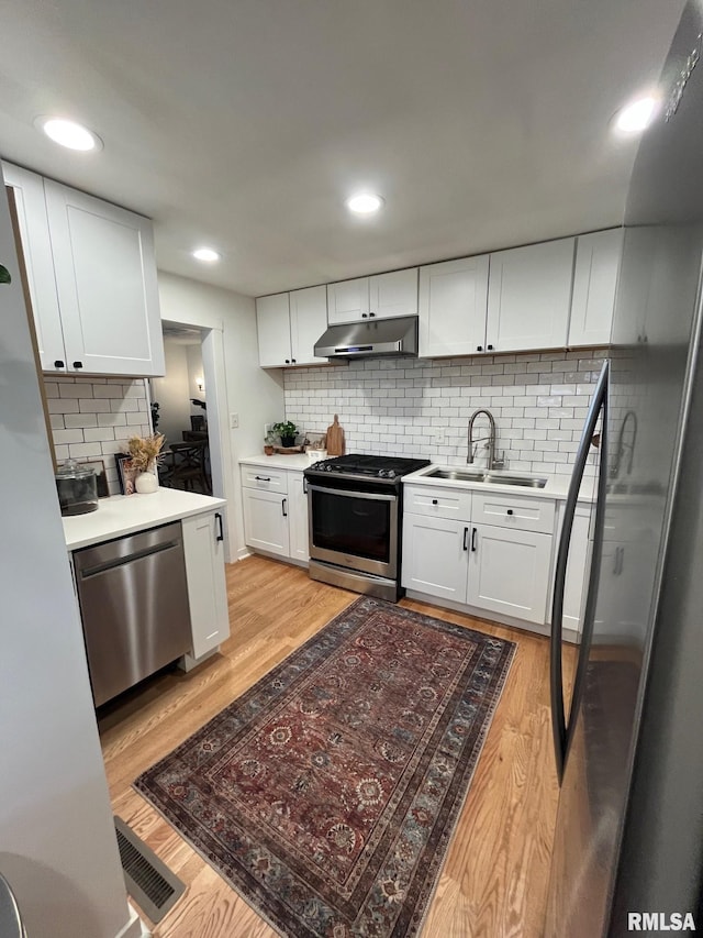 224 S Henderson St, Toulon, IL 61483 - kitchen with appliances with stainless steel finishes, under cabinet range hood, backsplash, light wood-style floors, and white cabinets
