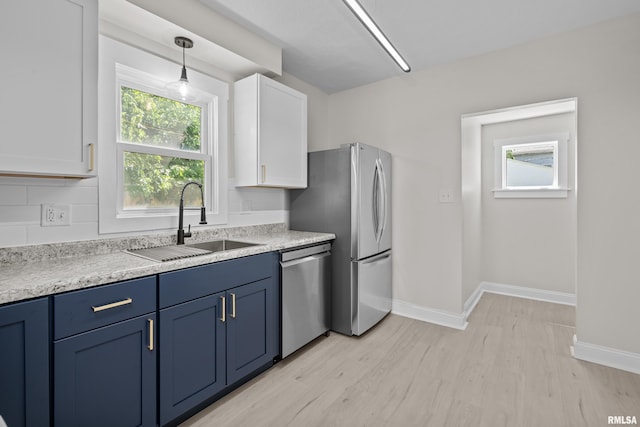 2664 Fair Ave, Davenport, IA 52803 - kitchen with appliances with stainless steel finishes, blue cabinets, white cabinets, light wood finished floors, and decorative backsplash