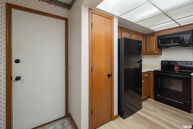 4554 Bunker Hill Dr, Bettendorf, IA 52722 - kitchen with black appliances, light wood-style floors, light countertops, brown cabinetry, and wallpapered walls