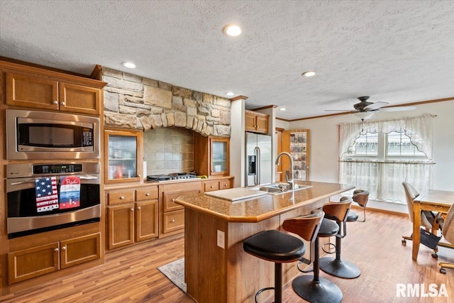 524 6th St, Andover, IL 61233 - kitchen featuring appliances with stainless steel finishes, brown cabinets, a textured ceiling, light wood-style floors, and a kitchen breakfast bar