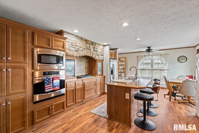 524 6th St, Andover, IL 61233 - kitchen featuring appliances with stainless steel finishes, brown cabinetry, a textured ceiling, light wood-style flooring, and a kitchen bar