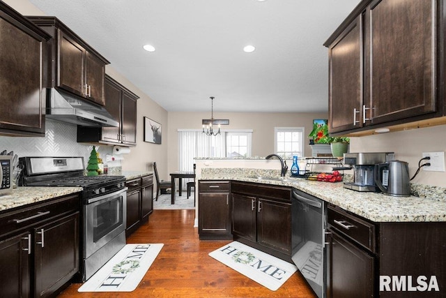 67 Cobblestone Ln, Le Claire, IA 52753 - kitchen with stainless steel appliances, under cabinet range hood, a peninsula, a chandelier, and dark brown cabinetry