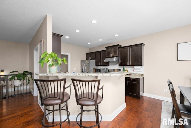 67 Cobblestone Ln, Le Claire, IA 52753 - kitchen with stainless steel fridge, under cabinet range hood, a breakfast bar, dark brown cabinets, and dark wood-style floors