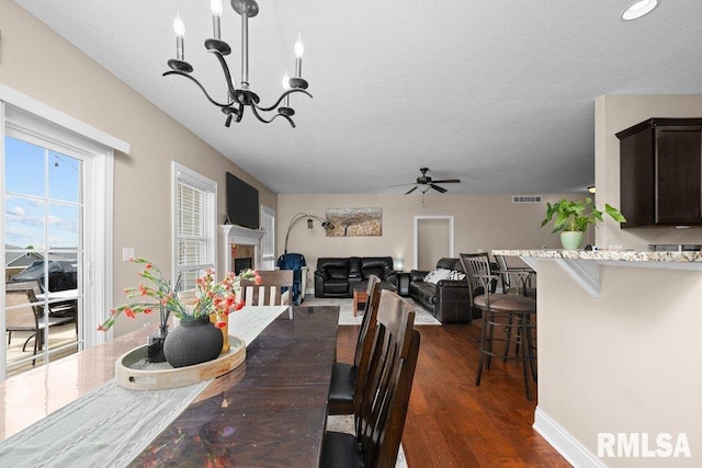 67 Cobblestone Ln, Le Claire, IA 52753 - dining room featuring ceiling fan, a textured ceiling, dark wood-style flooring, a chandelier, and a fireplace