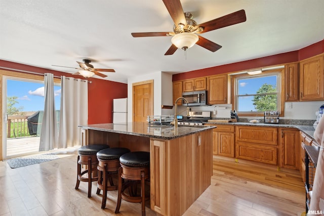 829 Union Ave, Lowden, IA 52255 - kitchen with stainless steel microwave, freestanding refrigerator, a center island with sink, dark stone countertops, and a kitchen breakfast bar