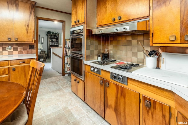 613 S Locust, West Frankfort, IL 62896 - kitchen with stainless steel double oven, light countertops, brown cabinetry, tasteful backsplash, and under cabinet range hood
