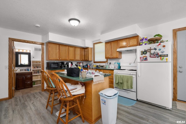 222 6th St, Buffalo, IA 52728 - kitchen with white appliances, light wood-style flooring, a center island, under cabinet range hood, and a kitchen bar