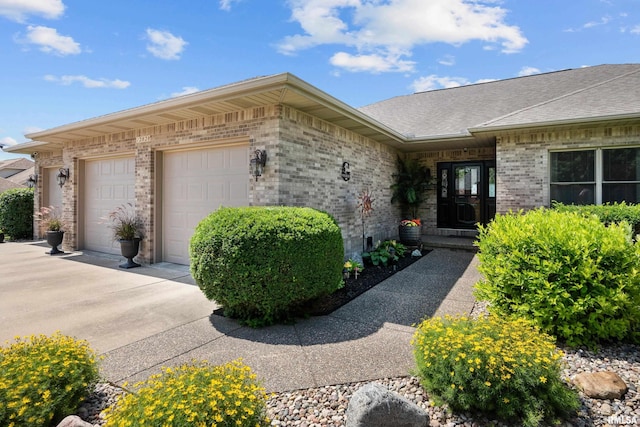 12828 25th Street Ct, Milan, IL 61264 - view of exterior entry featuring concrete driveway, brick siding, an attached garage, and a shingled roof