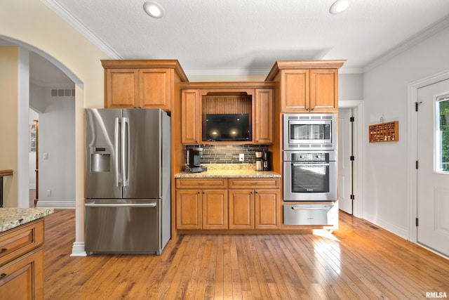 627 10th Ave, Silvis, IL 61282 - kitchen featuring appliances with stainless steel finishes, a warming drawer, brown cabinetry, arched walkways, and light wood-type flooring