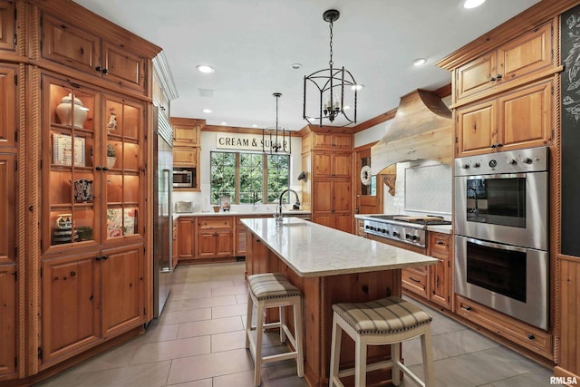 118 Ridgewood Ave, Davenport, IA 52803 - kitchen featuring appliances with stainless steel finishes, custom range hood, a chandelier, a center island with sink, and brown cabinetry