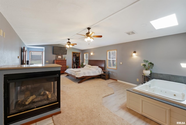 1217 7th St, De Witt, IA 52742 - bedroom featuring light wood-type flooring, lofted ceiling, a multi sided fireplace, a walk in closet, and a skylight