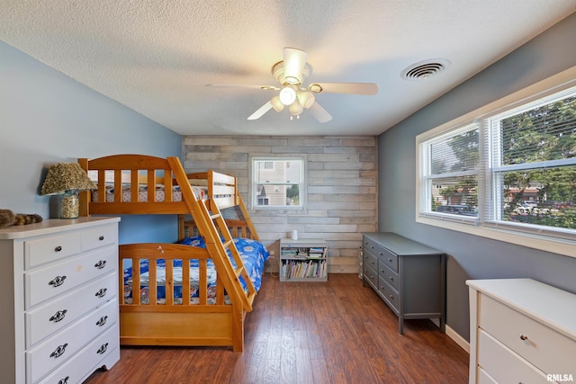 1217 7th St, De Witt, IA 52742 - bedroom featuring wooden walls, multiple windows, dark wood-style floors, a textured ceiling, and an accent wall
