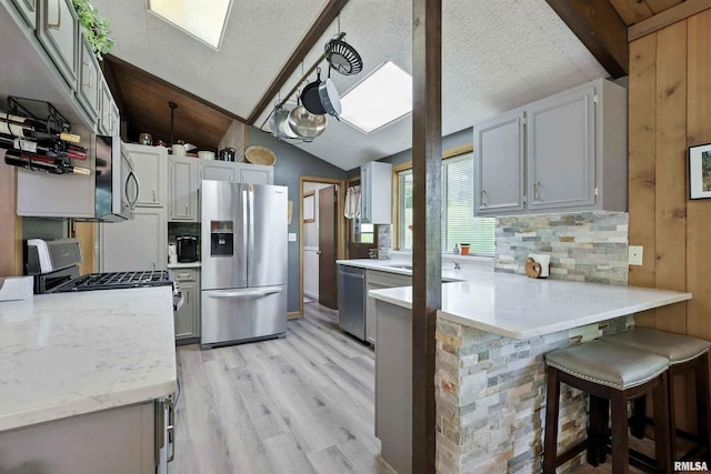 28002 230th St, Le Claire, IA 52753 - kitchen featuring stainless steel appliances, a peninsula, vaulted ceiling, light wood finished floors, and a kitchen bar