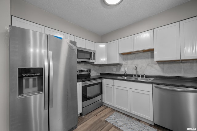 101 W Sheridan Dr, Eldridge, IA 52748 - kitchen featuring appliances with stainless steel finishes, dark countertops, white cabinetry, wood finished floors, and a textured ceiling