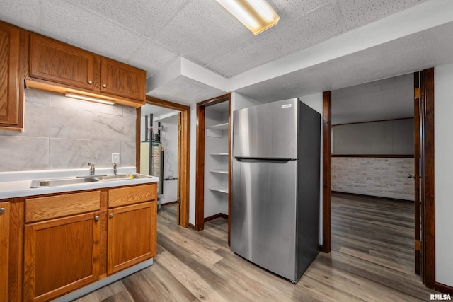 101 W Sheridan Dr, Eldridge, IA 52748 - kitchen featuring freestanding refrigerator, light wood-style flooring, brown cabinetry, water heater, and light countertops