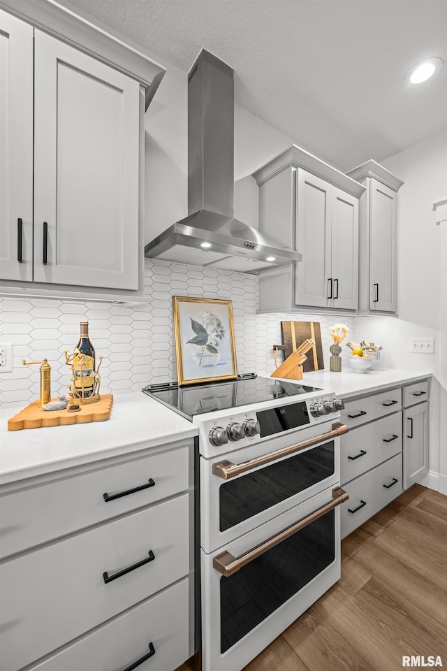 5835 Pigeon Creek Rd, Bettendorf, IA 52722 - kitchen featuring range with two ovens, wall chimney range hood, light countertops, wood finished floors, and decorative backsplash