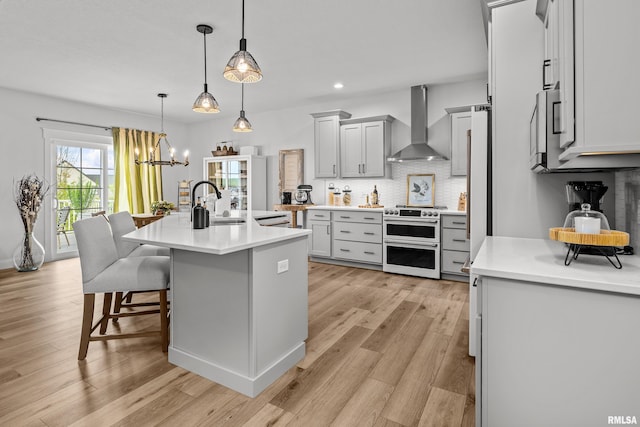 5835 Pigeon Creek Rd, Bettendorf, IA 52722 - kitchen featuring wall chimney range hood, range with two ovens, decorative backsplash, light countertops, and light wood-style flooring