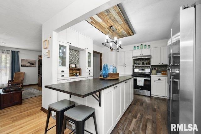 833 Robin Rd, Muscatine, IA 52761 - kitchen with appliances with stainless steel finishes, white cabinetry, wood finished floors, a chandelier, and a kitchen bar