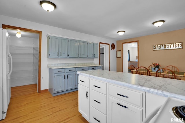 304 E Plum St, Anamosa, IA 52205 - kitchen with white fridge with ice dispenser, light wood-type flooring, light countertops, and blue cabinets
