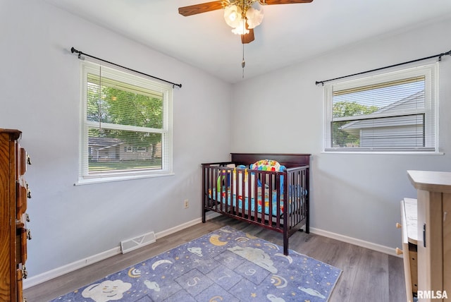 2506 Holly Dr, Bettendorf, IA 52722 - bedroom featuring multiple windows, wood finished floors, a crib, and ceiling fan