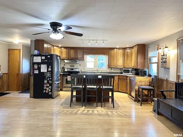 653 Ferry Rd, Miles, IA 52064 - kitchen featuring stainless steel appliances, brown cabinetry, ceiling fan, light wood-style flooring, and a wainscoted wall