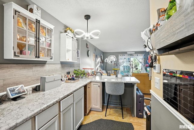 3295 Johnathan Ave, Bettendorf, IA 52722 - kitchen with a peninsula, glass insert cabinets, a chandelier, pendant lighting, and light stone counters