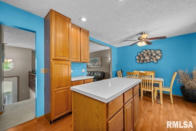 2401 W Dale Ct, Bettendorf, IA 52722 - kitchen featuring a textured ceiling, ceiling fan, light countertops, light wood-style flooring, and a kitchen island