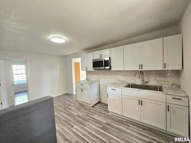 1912 Breese St, Muscatine, IA 52761 - kitchen featuring stainless steel microwave, tasteful backsplash, light wood-type flooring, white cabinetry, and a textured ceiling
