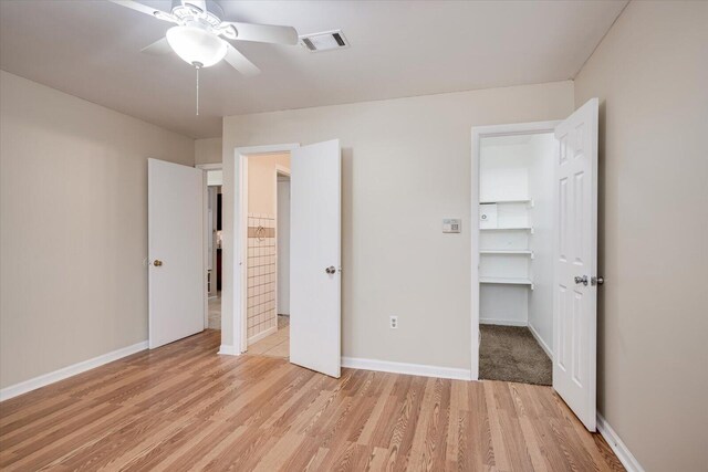 unfurnished bedroom with ceiling fan, a walk in closet, and light hardwood / wood-style flooring