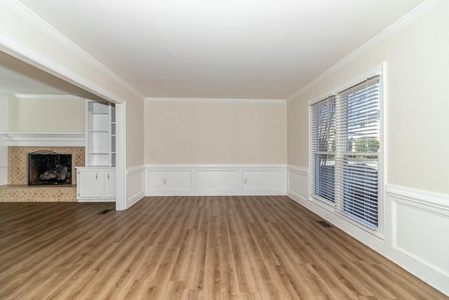 unfurnished living room with built in features, a fireplace, crown molding, and light hardwood / wood-style floors