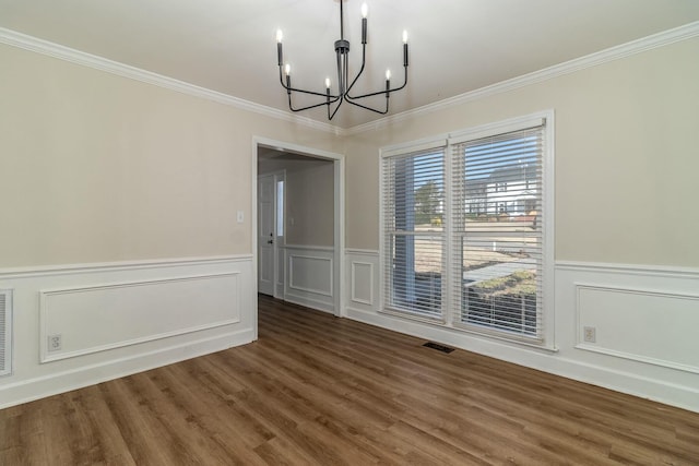 unfurnished dining area featuring dark hardwood / wood-style floors, crown molding, and an inviting chandelier