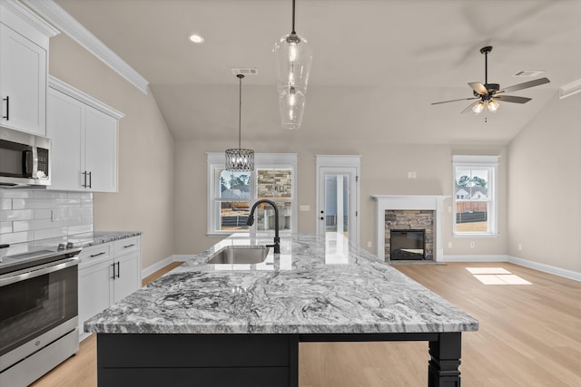 kitchen with a sink, appliances with stainless steel finishes, light wood-style floors, decorative backsplash, and lofted ceiling