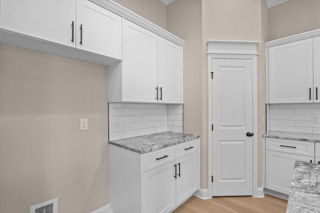 kitchen with white cabinetry, light wood finished floors, tasteful backsplash, and light stone counters