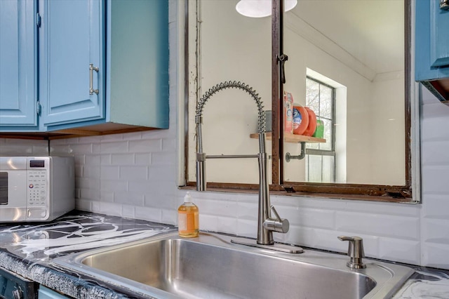 details featuring blue cabinetry, ornamental molding, backsplash, a sink, and white microwave