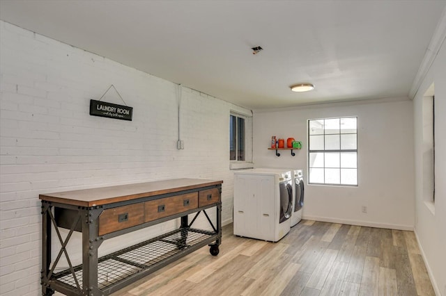 clothes washing area with baseboards, light wood-style floors, brick wall, washer and dryer, and laundry area