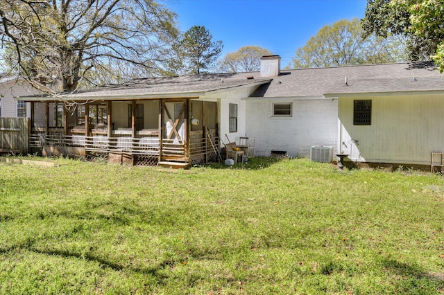 rear view of property featuring central AC unit, a chimney, brick siding, a lawn, and a shingled roof