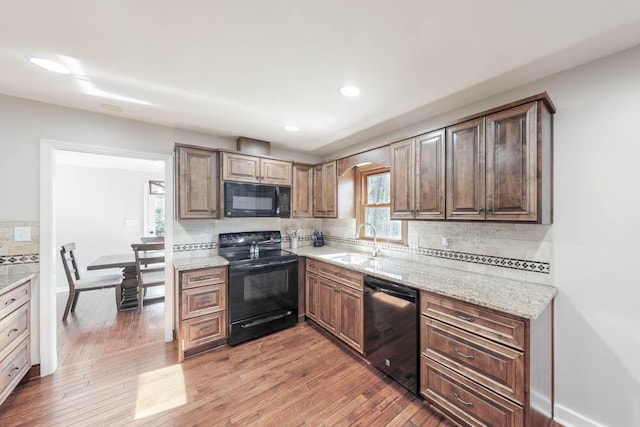 kitchen with sink, wood-type flooring, black appliances, light stone countertops, and backsplash