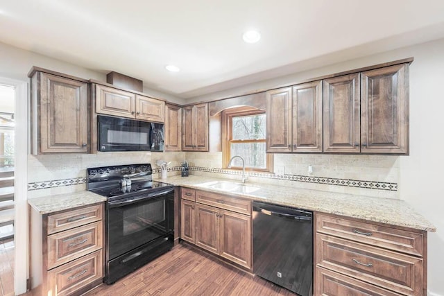 kitchen with sink, hardwood / wood-style floors, light stone counters, black appliances, and decorative backsplash