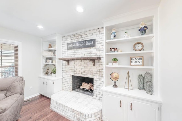 living room with built in shelves, a fireplace, and light hardwood / wood-style flooring