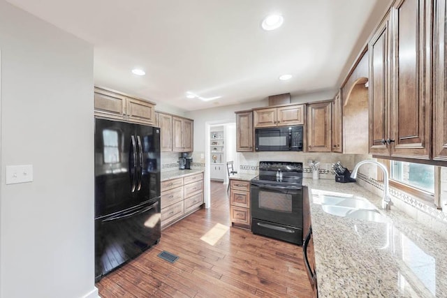 kitchen featuring dark hardwood / wood-style floors, sink, decorative backsplash, black appliances, and light stone countertops