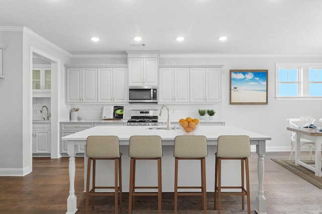 kitchen with appliances with stainless steel finishes, a kitchen island with sink, white cabinets, light countertops, and a sink