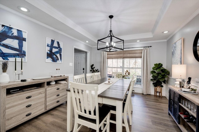 dining area featuring a notable chandelier, a tray ceiling, dark wood-type flooring, and ornamental molding